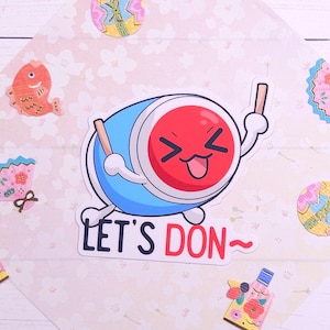 May include: A cartoon illustration of a red and blue drum with a smiling face and the text "Let's Don~" on a pink background with various Japanese-themed decorations.