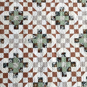 May include: A quilt with a geometric pattern in shades of brown, white, and green. The quilt is made up of squares and triangles, and the pattern is repeated throughout the quilt.