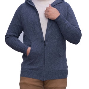 Könnte beinhalten: Dunkelblauer Kapuzenpullover mit Reißverschluss, Kapuze mit Kordelzug und gerippten Bündchen und Saum. Der Hoodie hat einen durchgehenden Reißverschluss und zwei Vordertaschen. Darunter wird ein cremefarbener Rollkragenpullover getragen.