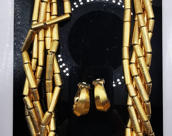 May include: A gold-toned necklace and earrings set. The necklace is made of multiple strands of linked gold-toned cylinders. The earrings are hoop-shaped with a textured surface.