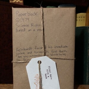 Op de afbeelding: Een bruin papieren pakketje dat is ingepakt met touw en een wit label met de tekst "Blind date with a book". Het pakket is gelabeld met "Paperback 1979 Science Fiction Based on a movie".