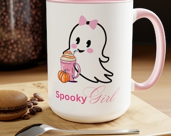 Puede incluir: Taza de cerámica blanca con borde y asa de color rosa. La taza presenta un fantasma de dibujos animados con un lazo rosa y bebiendo un latte de especias de calabaza rosa. El texto "Spooky Girl" está escrito en rosa debajo del fantasma.