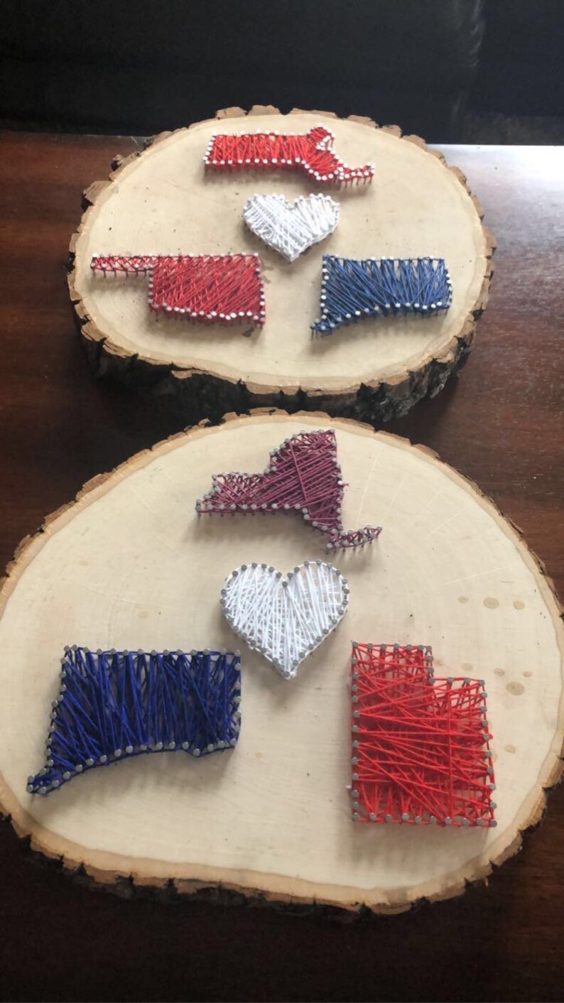 K&ouml;nnte beinhalten: Zwei Holzscheiben mit String Art von verschiedenen Bundesstaaten und Herzen. Die obere Scheibe zeigt String Art in Rot, Wei&szlig; und Blau von Massachusetts, Oklahoma und Connecticut. Die untere Scheibe zeigt String Art in Rot, Wei&szlig; und Blau von New York, Connecticut und Utah.
