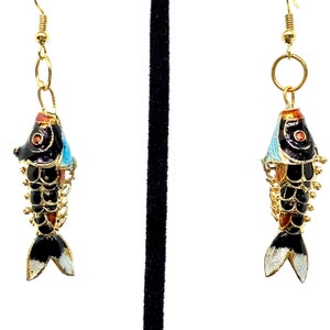 May include: A pair of gold-tone earrings featuring black and white enamel fish with red and blue accents. The fish are detailed with scales and fins.