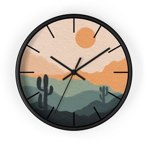 May include: A round wall clock with a black frame. The clock face features a desert landscape with a sun, mountains, and cacti in shades of orange, green, and beige. The clock hands are black.