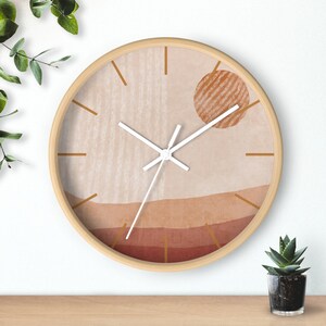 May include: A round wooden wall clock with a white face and gold hands. The clock face features a beige and brown abstract design with a sun-like shape in the center.