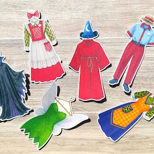 May include: A collection of colorful, die-cut paper costume pieces, including a red and white dress, a red robe with a blue wizard hat, a blue and red uniform, a green fairy costume, and a black cape.