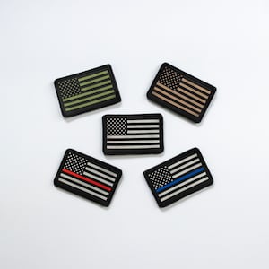 May include: Five rectangular patches featuring the American flag design. The patches are black with variations in the flag's colors, including green, tan, and a black and white design. Two patches have a red and blue stripe.