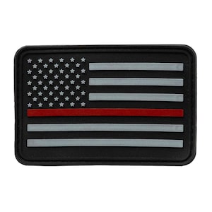 May include: A rectangular patch featuring a stylized American flag design. The flag has a black background, gray stripes, white stars, and a red stripe. The patch has a black border.
