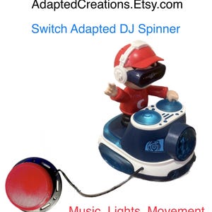 Może przedstawiać: Zabawka Switch Adapted DJ Spinner z czerwonym przyciskiem i figurką DJ-a w czerwonej czapce i słuchawkach. Zabawka jest niebiesko-biała ze światłami i tekstem "Music, Lights, Movement". Nazwa sklepu Etsy to "AdaptedCreations.Etsy.com".