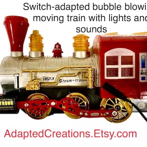 Puede incluir: Un tren de juguete rojo, plateado y dorado con una función de soplado de burbujas. El tren tiene luces y sonidos y dice "1823 Steam-train".