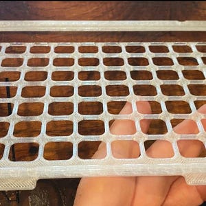 May include: A white plastic grid with a rectangular shape. The grid has many small squares.