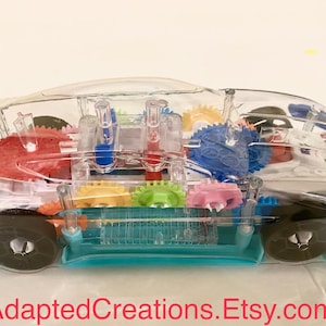 May include: A clear plastic toy car with colorful gears and a blue base. The car has a transparent body that reveals the inner workings of the toy.