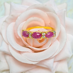 Op de afbeelding: Een gouden ring met vijf ovale roze edelstenen en kleine heldere edelstenen gezet in een gouden band.
