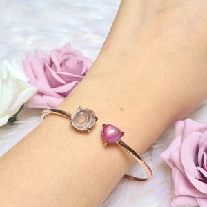Op de afbeelding: Een gouden armband met een rozenkwarts en een roze hartvormige edelsteen. De armband wordt om de pols gedragen.