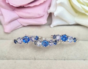 Puede incluir: Tres anillos de plata con piedras preciosas azules y moradas. Los anillos están dispuestos en una fila sobre una superficie gris claro.