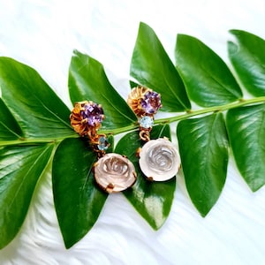 May include: A pair of gold earrings with carved rose quartz stones and amethyst and blue topaz accents.