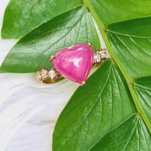 May include: A heart-shaped pink gemstone ring with a gold band and small diamonds set around the stone.