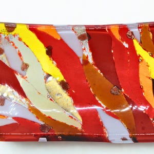 以下が含まれることがあります： 鮮やかな抽象デザインの長方形ガラス皿。赤、黄、オレンジ、白の色が混ざり合い、金色のフレークが散りばめられています。縁は丸みを帯びており、全体的なデザインは芸術的で装飾的です。