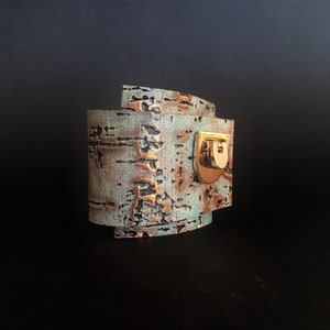 Könnte beinhalten: Ein blaues und braunes Lederarmband mit einem goldenen Verschluss. Das Armband hat einen Used-Look und ist aus strukturiertem Leder gefertigt.