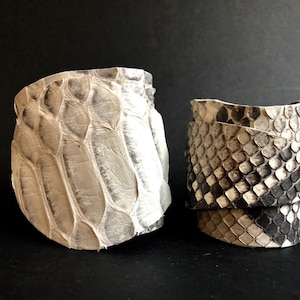 Peut inclure: Deux bracelets en cuir avec un motif de peau de serpent. Un bracelet est blanc et l'autre est brun et blanc.