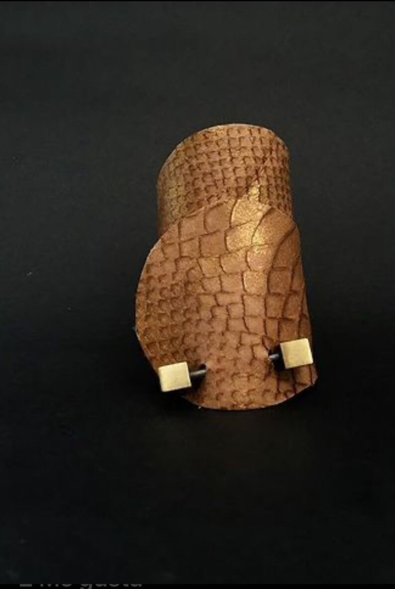 May include: A brown leather cuff bracelet with a textured snakeskin pattern and two gold square accents.