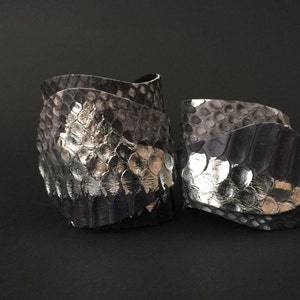 May include: Two silver and black snake skin bracelets. The bracelets are made of leather and have a textured surface.