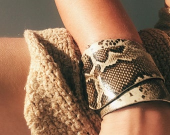 Könnte beinhalten: Ein braunes und weißes Schlangenleder-Armband mit einem strukturierten Muster.
