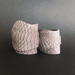 Könnte beinhalten: Zwei graue Lederarmbänder mit Schlangenhautmuster.