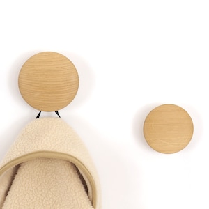 Op de afbeelding: Twee houten wandhaken met een lichtbruine afwerking. Aan één haak hangt een wit fleecejack.