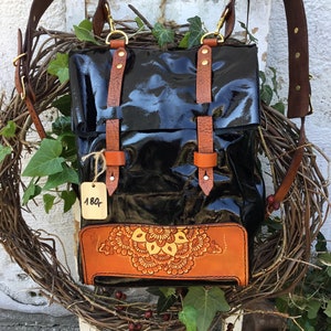 May include: Black leather satchel with brown leather straps and a decorative orange mandala design. The bag has a price tag that says "180".