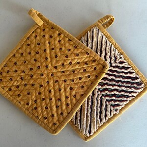 May include: Two yellow quilted pot holders. One has a floral pattern and the other has a wavy pattern.
