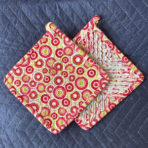 May include: Two red and green pot holders. One has a circle pattern and the other has a striped pattern.