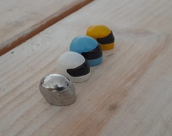 May include: Four miniature helmets in different colors: silver, white, light blue, and yellow. Each helmet has a black visor.