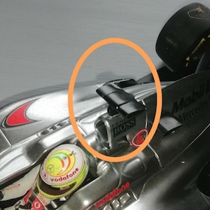May include: A close-up of a silver racing car with a black wing on the back. The car has a black and silver "BOSS" logo on the side. The car is on a black surface.
