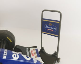 Peut inclure: Modèle de voiture de course de Formule 1 bleu et blanc avec les mots "Renault" et "Sanyo" sur le côté. La voiture est sur un présentoir avec une pancarte bleue et jaune qui dit "Rothmans Racing".