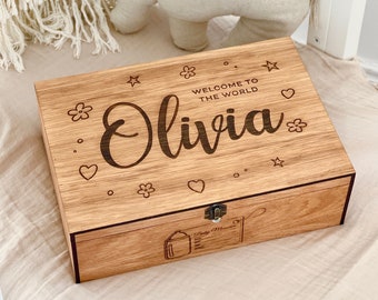 May include: Wooden keepsake box with a hinged lid, engraved with the text "Welcome to the world Olivia" and decorated with hearts, stars, and flowers. The box has a latch and a small compartment on the inside.