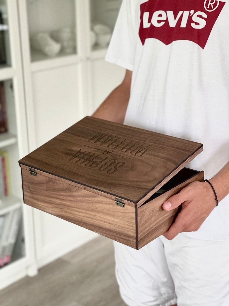 K&ouml;nnte beinhalten: Eine Holzkiste mit einem Scharnierdeckel. Der Deckel ist ge&ouml;ffnet und die Kiste ist mit dem Text "Presents & Wishes" graviert.