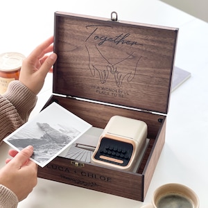 May include: A wooden keepsake box with the word "Together" and a line drawing of two hands holding each other. The box contains a small beige and gold label maker, a black and white photo, and is labeled "LUCA + CHLOE". A cup of coffee sits nearby.