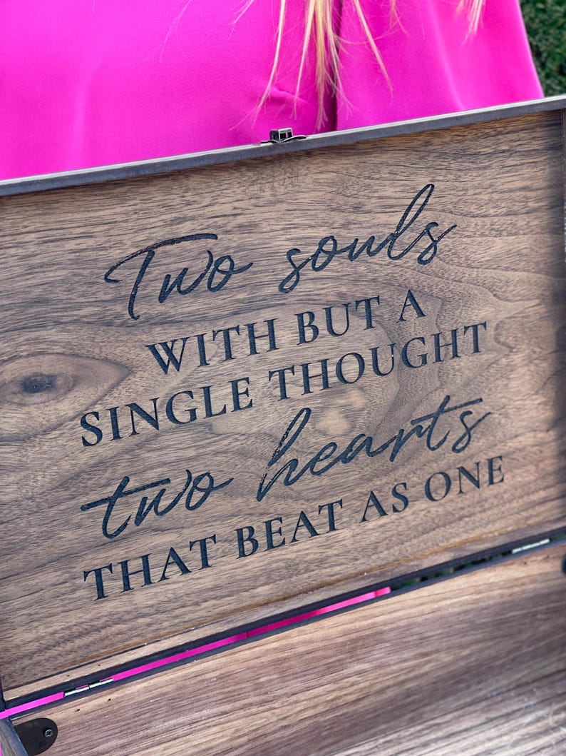Pu&ograve; includere: Un cofanetto in legno scuro con l'iscrizione "Two souls with but a single thought two hearts that beat as one" in corsivo nero. Il cofanetto ha una cerniera in metallo e un accento rosa.