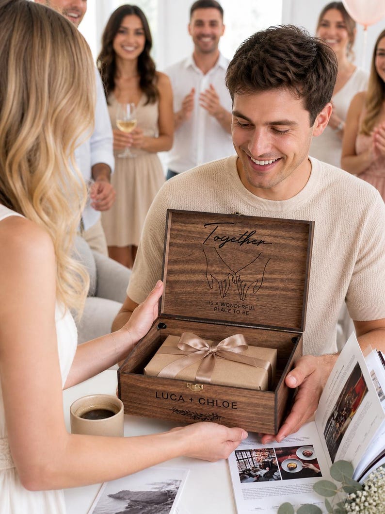 May include: A wooden keepsake box with a gift inside, tied with a satin bow. The box is engraved with the word "Together" and the names "Luca + Chloe". The box is being opened by a person, with a group of people in the background.