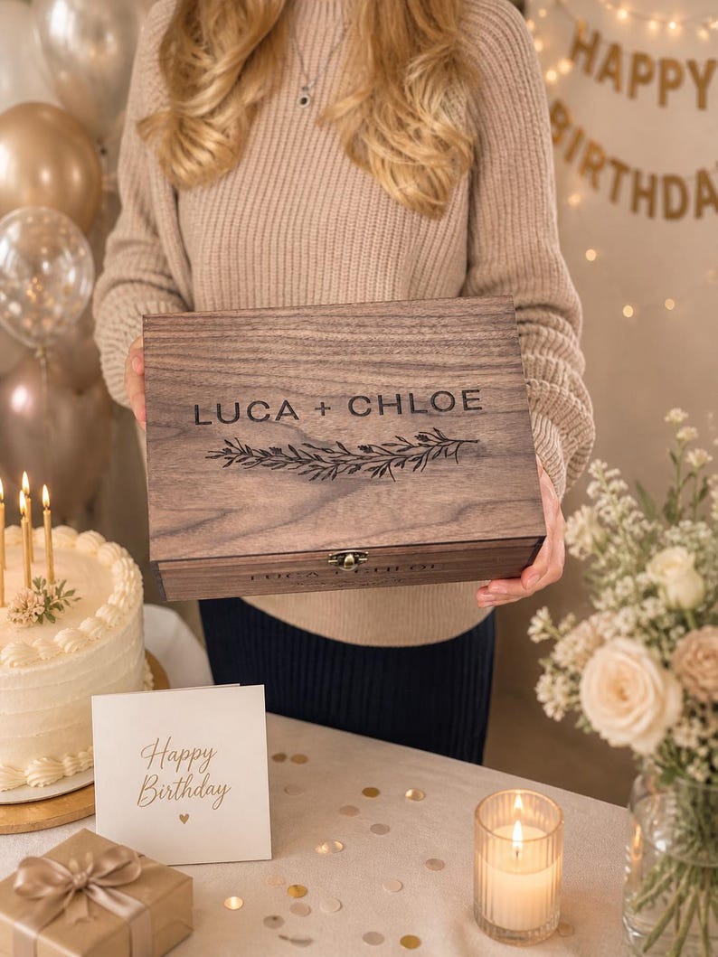 May include: A wooden box with the names "LUCA + CHLOE" engraved on the lid, along with a floral design. The box is held in front of a birthday scene with a cake, a "Happy Birthday" sign, and a gift box.