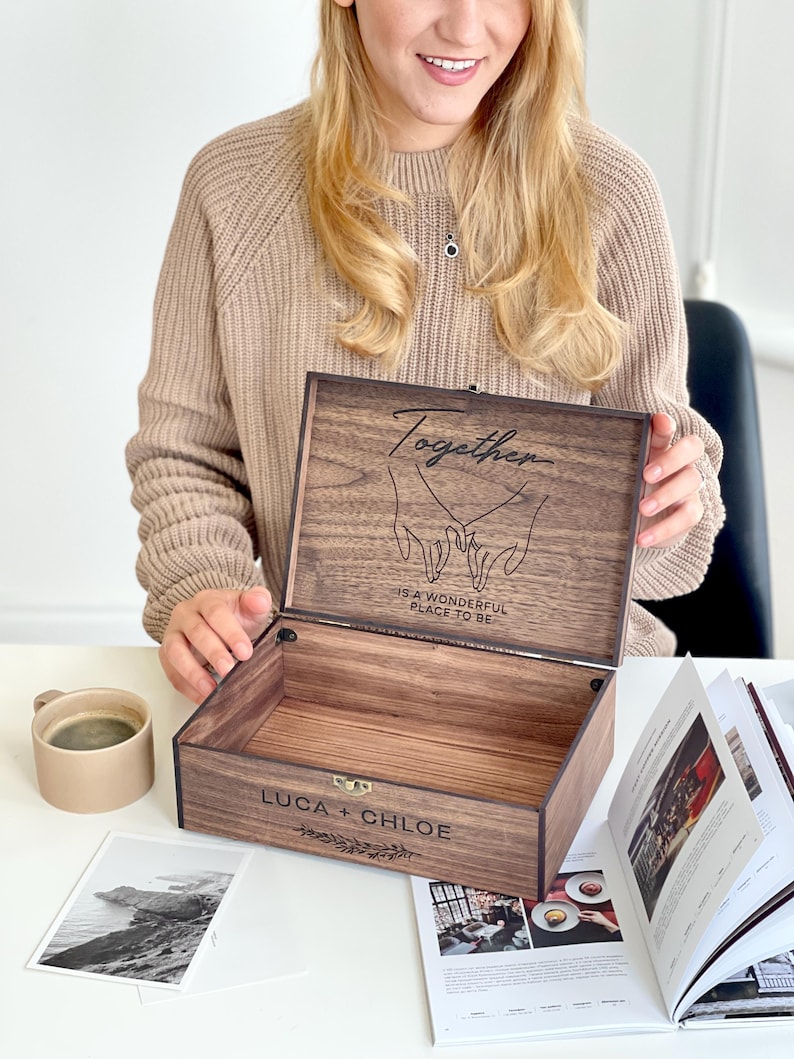 May include: A wooden keepsake box with the lid open, revealing the interior. The lid is engraved with the word "Together" and a graphic of two hands holding each other. The box also has the names "LUCA + CHLOE" engraved on the front.