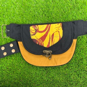 Puede incluir: Un bolso de cintura negro y amarillo mostaza con una solapa decorativa con un diseño amarillo y rojo. El bolso tiene una hebilla y un cierre a presión de latón, y una correa ajustable a juego. Un accesorio elegante.