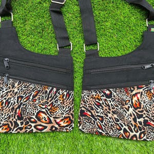 Puede incluir: Dos bolsos cruzados negros con detalles de estampado de leopardo. Cada bolso tiene dos bolsillos con cremallera y una correa negra ajustable. El estampado de leopardo incluye tonos marrones, naranjas y crema.