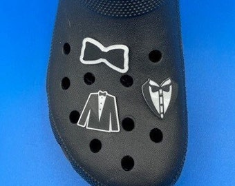 May include: Black and white tuxedo and bow tie shoe charms. The charms are attached to a black clog shoe.