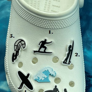 May include: White shoe with various black and blue surfing themed shoe charms. The charms include a surfer, a wave, a surfboard, and a kite surfer. The charms are numbered 1 through 5.