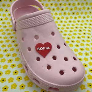 May include: Pink Crocs with a red heart charm that says "SOFIA" on it.