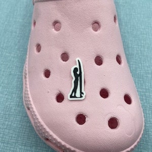 May include: A pink shoe with a black and white sticker of a person surfing. The sticker is on the top of the shoe.