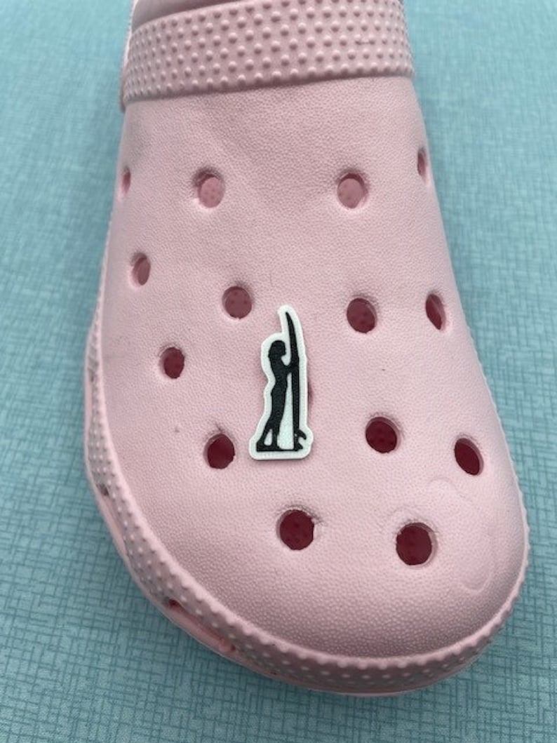 May include: A pink shoe with a black and white sticker of a person surfing. The sticker is on the top of the shoe.